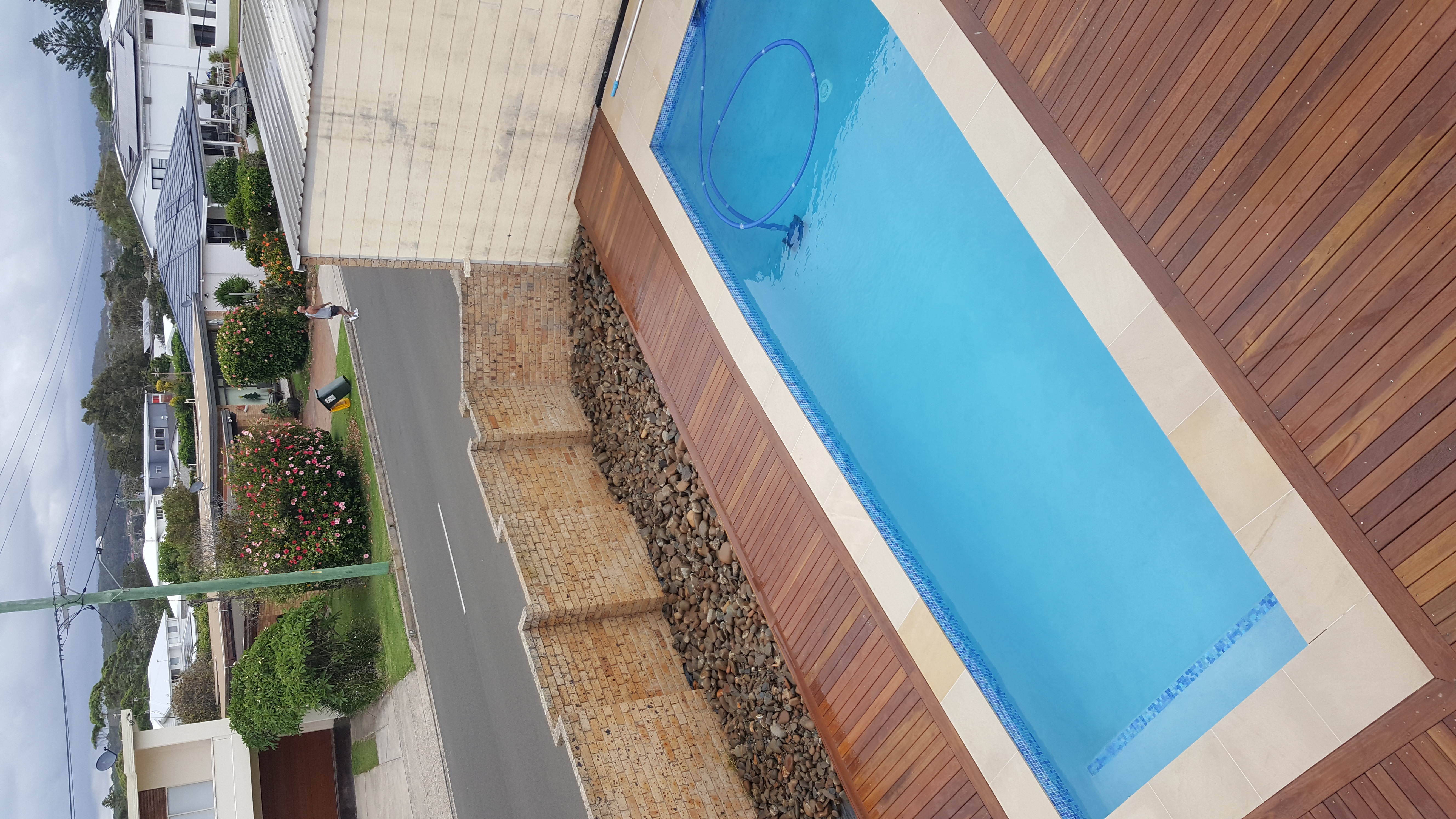 A timber deck surrounding a clear rectangular pool in the yard of a home next to a street
